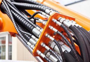 Industrial hydraulic hoses equipped with black spiral hose-spring-guard protection systems connected to orange compact power unit machinery.